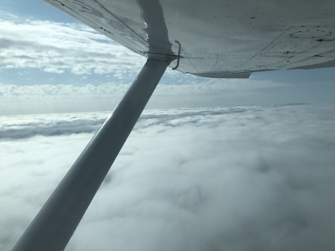 A view of clouds out the window beneath the wing structure of a small airplane.