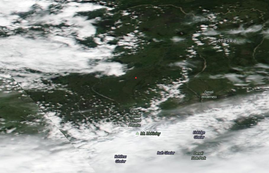 A satellite view of the area around Denali National Park and Preserve in Alaska. The land is dark green, except where it's covered by white clouds at the bottom and upper left of the image. One stark red dot stands out in the middle of the image.