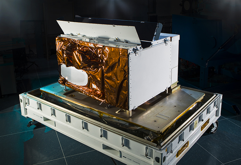 The VIIRS instrument, a large square box constructed of white metal and copper foil, sits against a black backdrop in Raytheon Intelligence & Space's El Segundo, California, facility.