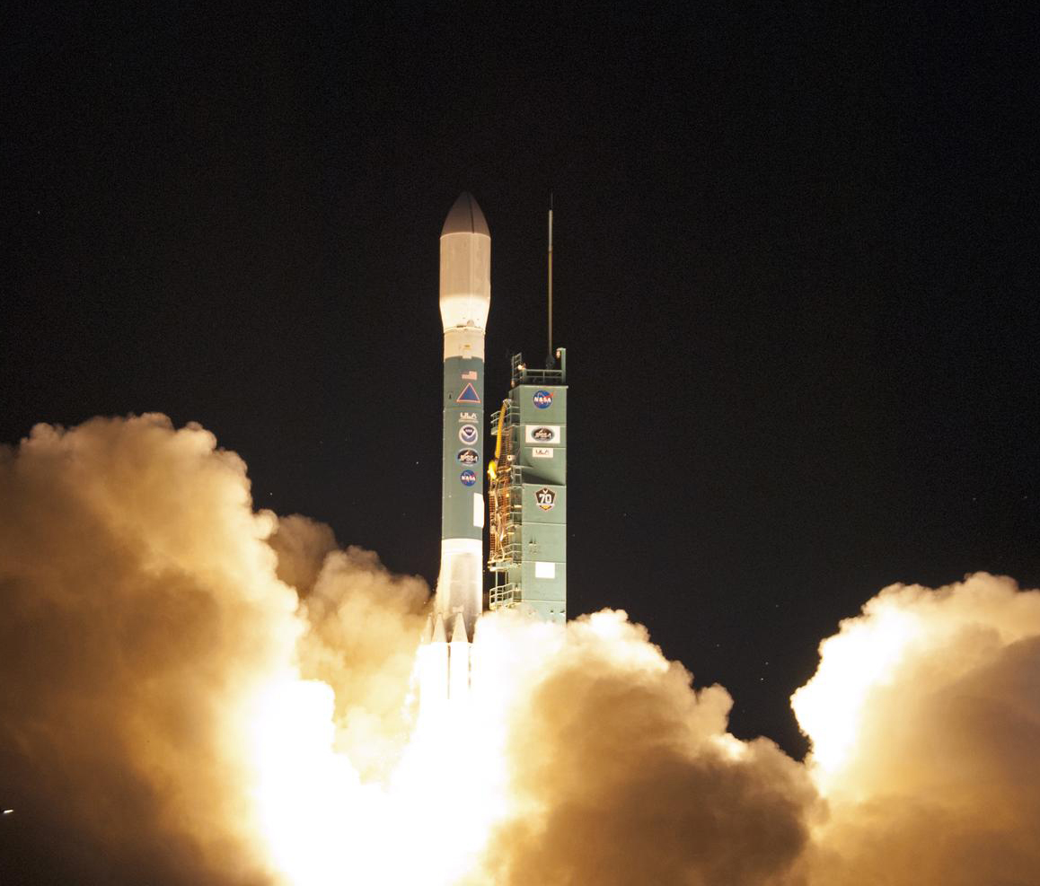 A tall rocket sits on the launch stand, partially obscured by large clouds of white smoke as it prepares to take off.