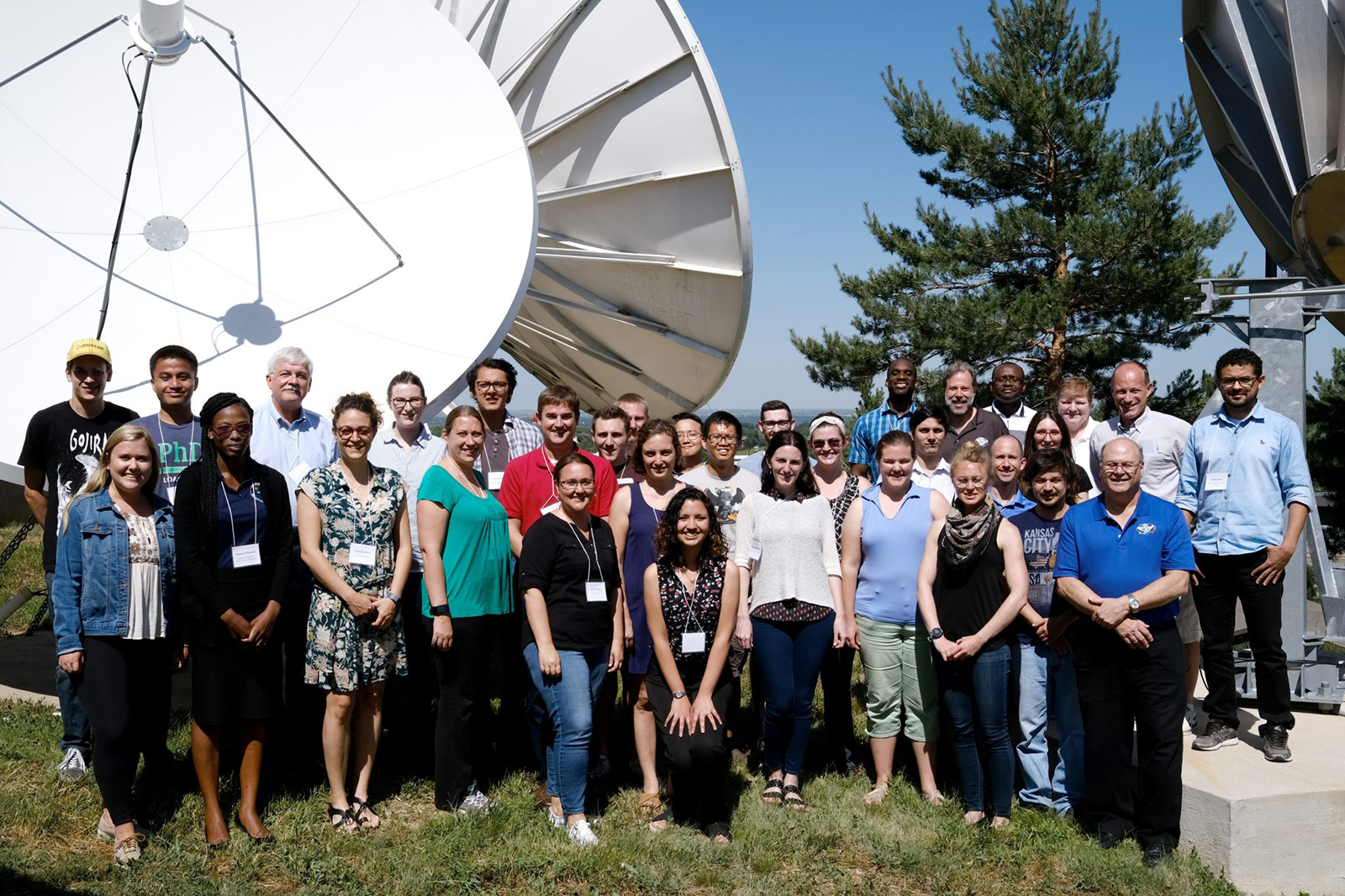A group of about 20 people stands in front of an antenna at the CIRA NOAA/NASA Satellite Meteorology Summer Workshop.