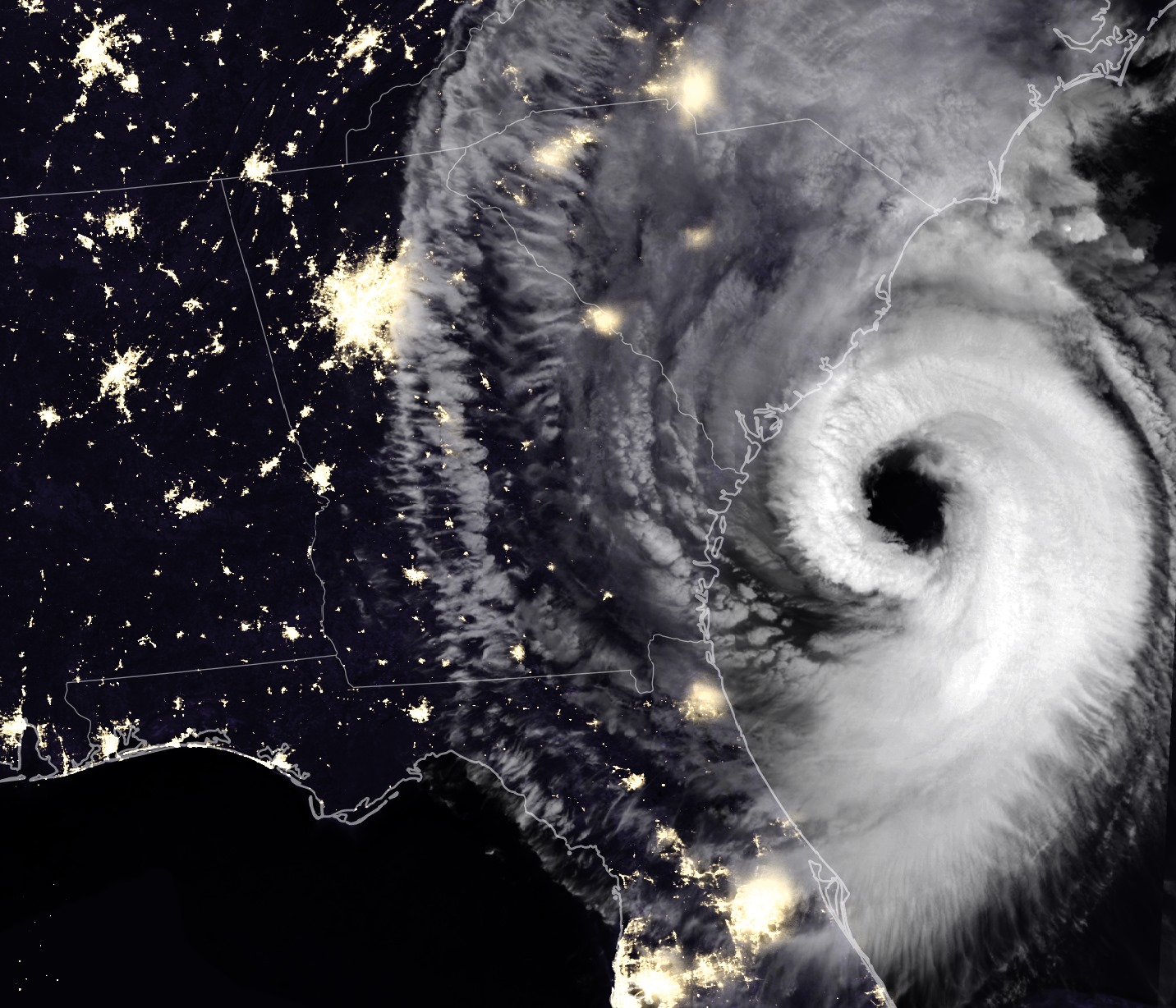 On a satellite map of the southeastern U.S. coast at night, city lights glow against a blue back drop on the left, while the huge swirling white clouds of Hurricane Dorian loom on the right, near the coast of South Carolina.