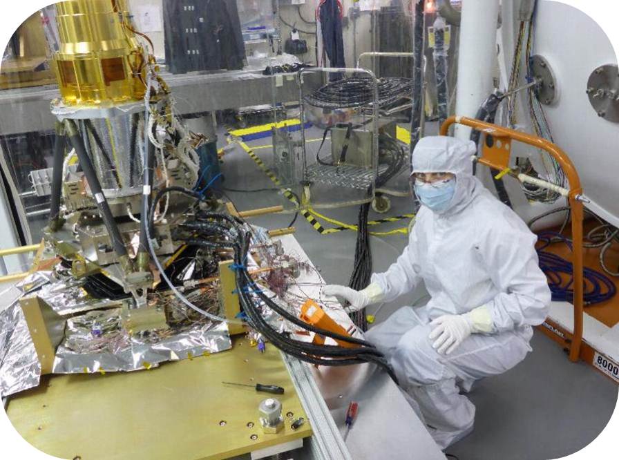 Engineer in white protective suit looks at camera while working on the GLM.