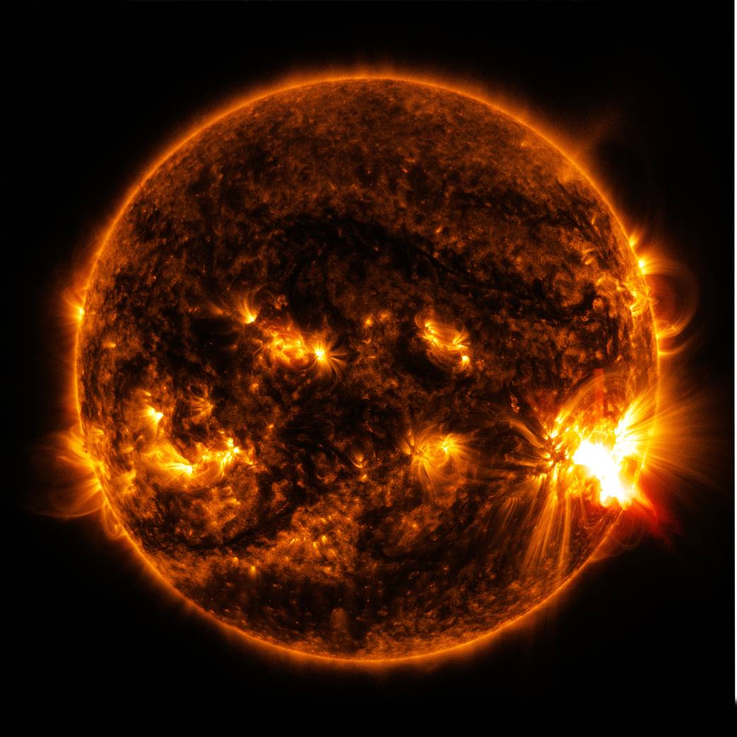 Close up image of a dark sun with a very bright solar flare and several other smaller bright spots.