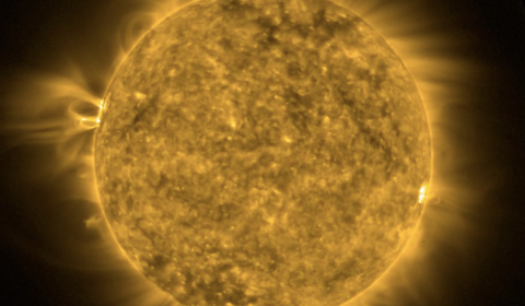 A telescopic image of the Sun zoomed to fill the screen. Colored a false green to identify the image as taken at a wavelength of 94 Angstroms to show 6 million degree plasma from the solar corona. Mottled with bright spots and dark regions, a bright spot just right of center stands out. This spot is the location of a solar flare which heats coronal plasma to millions of degrees revealing the magnetic field loops responsible for the solar flare.