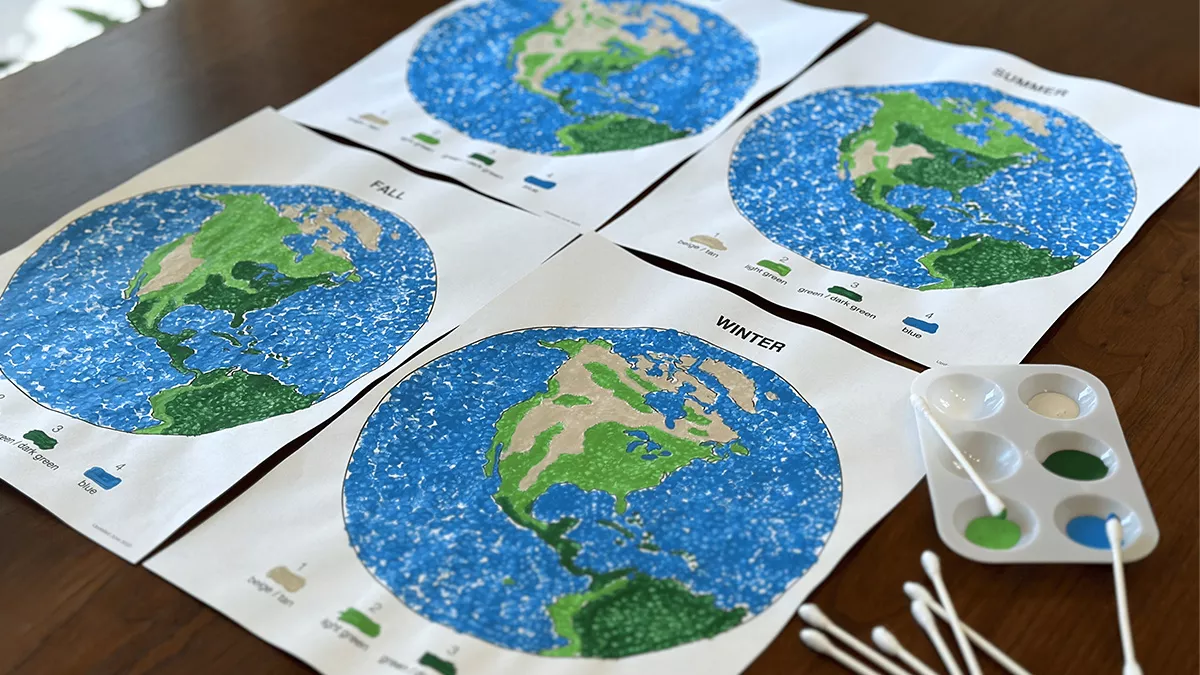 Photo of four color maps of the Earth on a tabletop, with a dish with paint