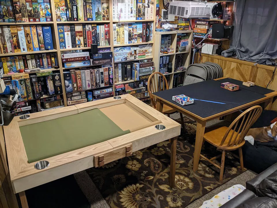 A view of a room in Joseph's house where there are two large game tables. Behind them are shelves with hundreds of board games on them.