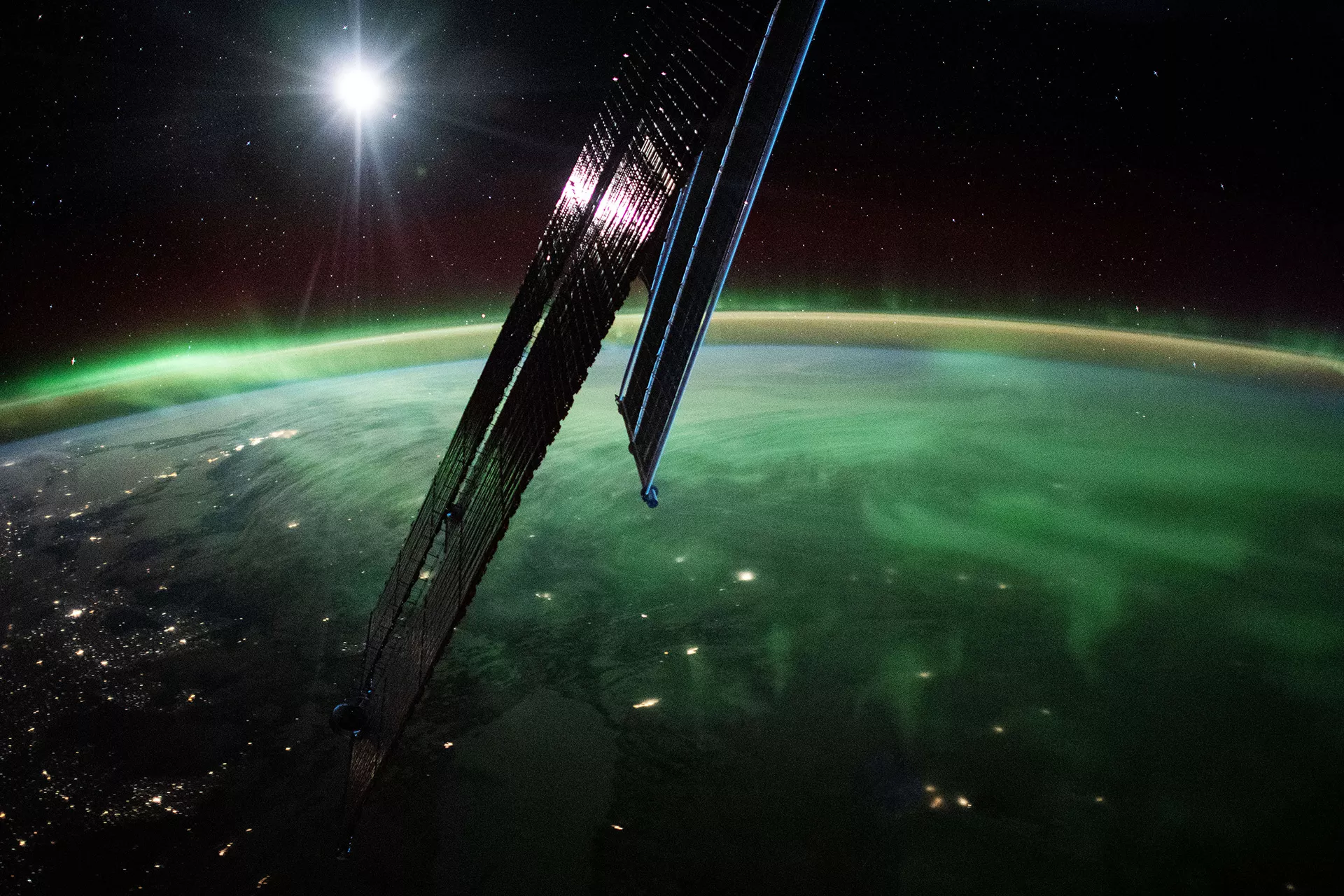 Photo from space of the Earth's horizon illuminated with colorful streaks of light. Parts of the spacecraft's solar arrays are visible in the foreground.