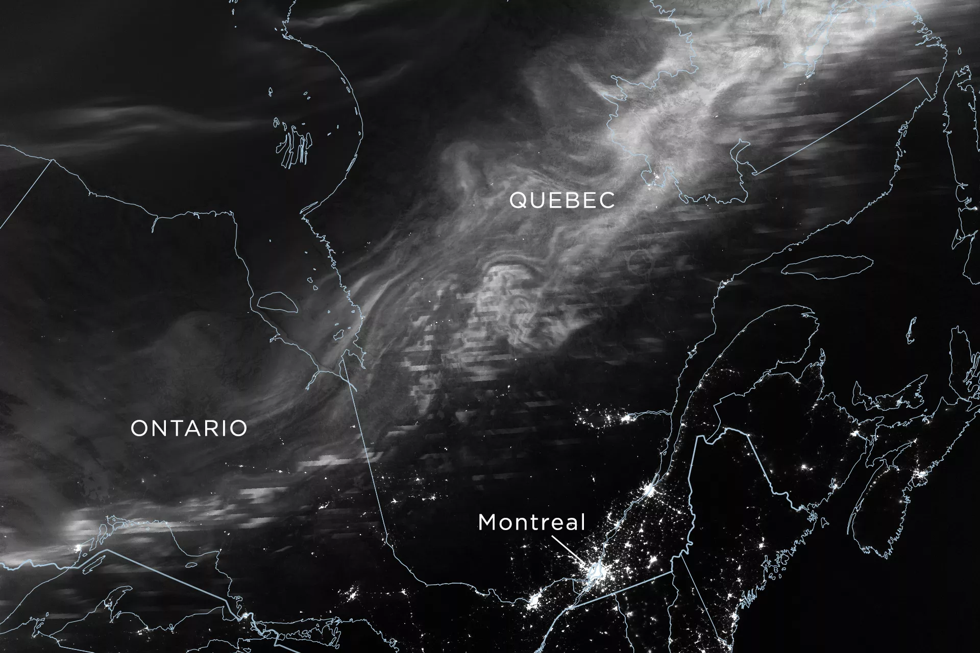 A greyscale satellite image over map contours of regions in Northeastern US and Canada, capturing the illumination from the aurora. 