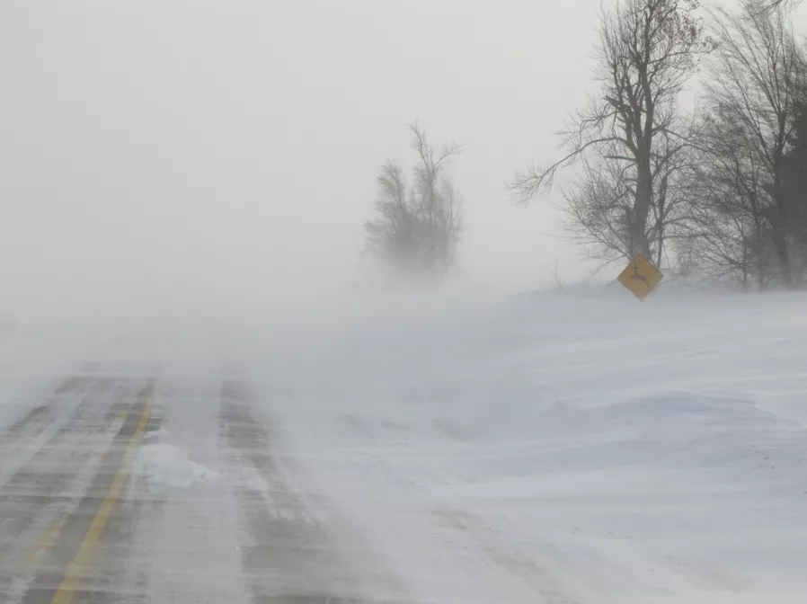 A photograph of heay snow blowing across a road during blizzard conditions in rural Iowa