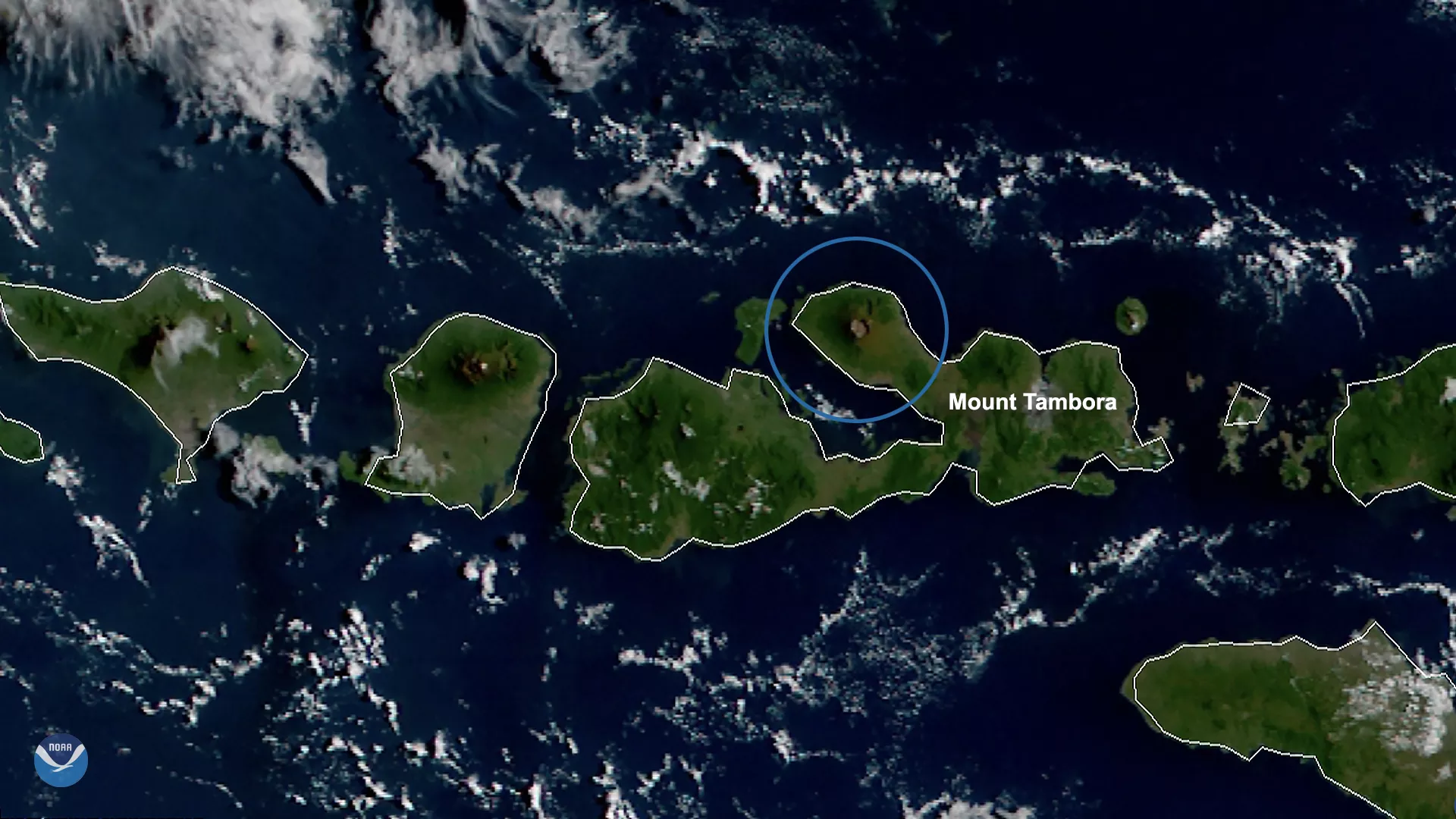 Green islands of Indonesia shown surrounded by dark blue ocean with white clouds above. Mount Tambora is circled in blue. 