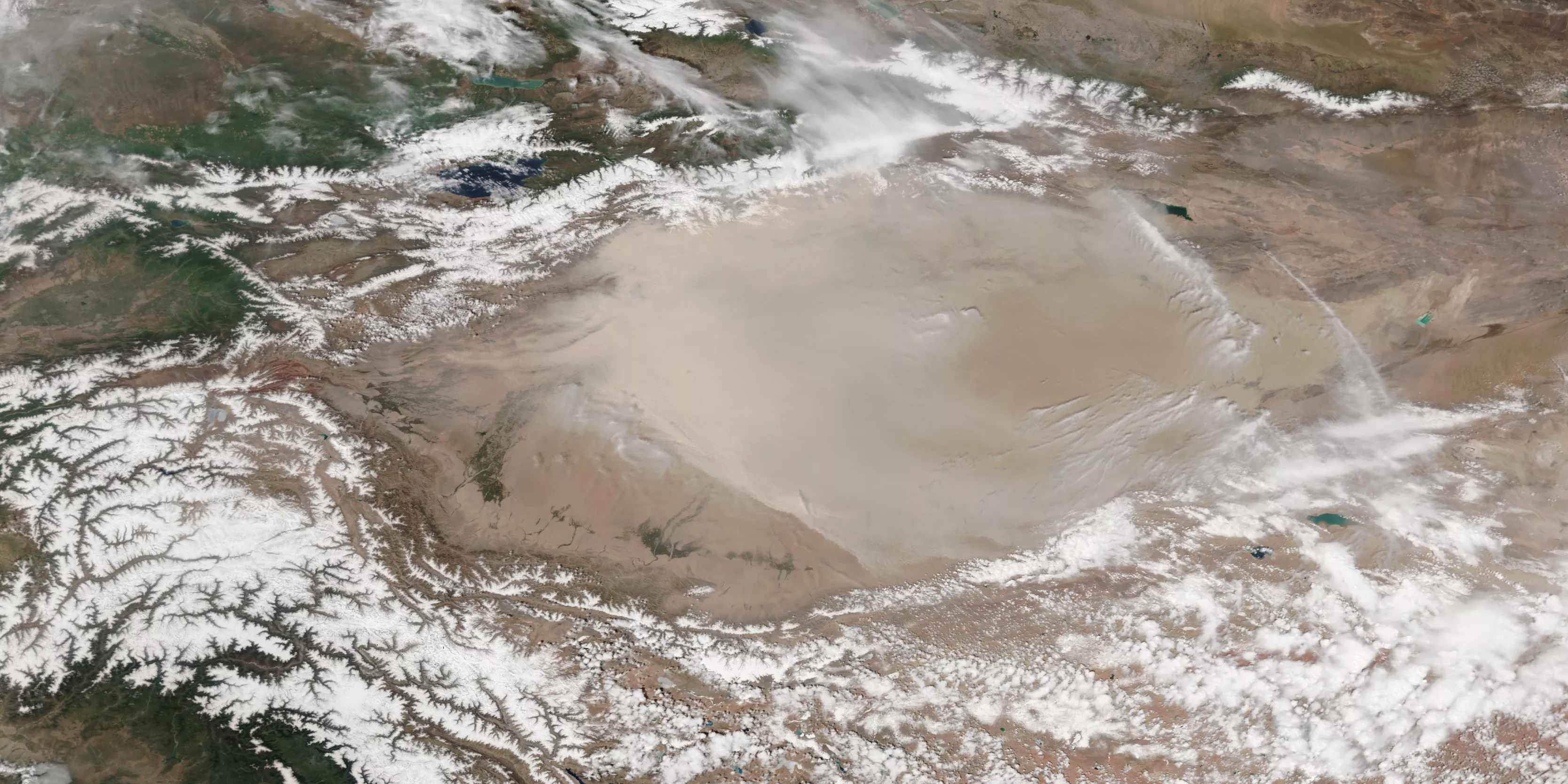 A true-color image of the Taklimakan Desert in China showing a light beige dust cloud over a similarly colored background