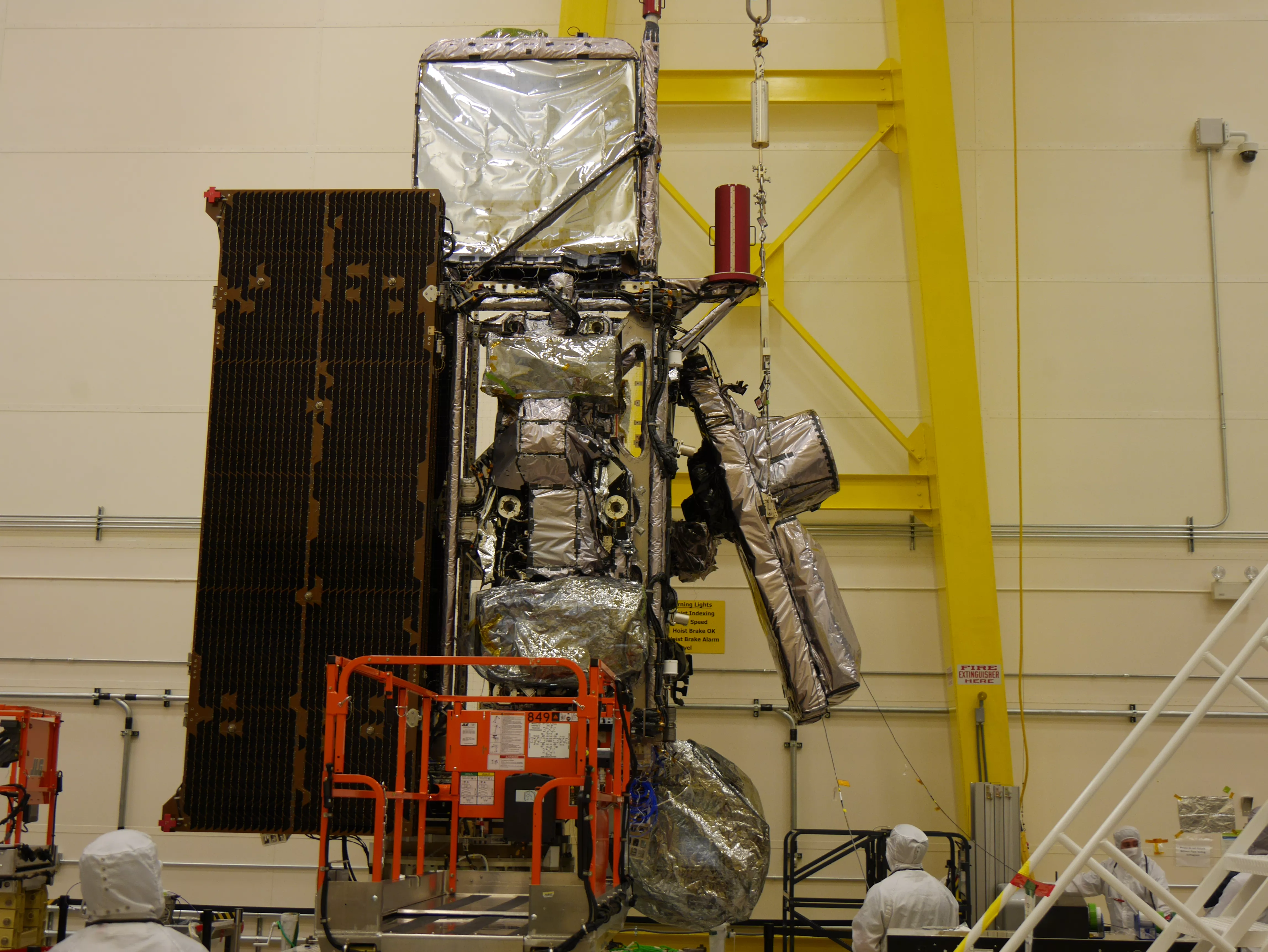 Photo of a clean room and a satellite array, with suited workers all around its perimeter.