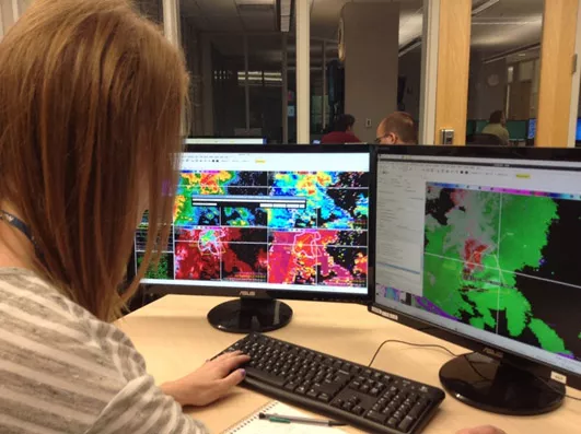 Photo of woman at computer terminal, studying weather outputs.