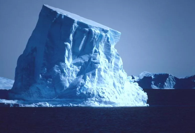 Photograph of large iceberg in middle of body of water.
