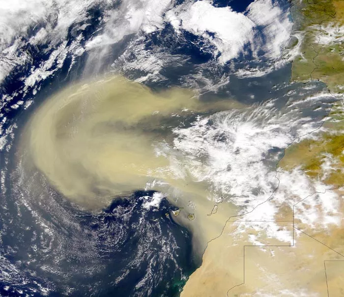 A satellite image of the northwestern coast of Africa shows a heavy beige cloud of dust wafting over the Atlantic Ocean