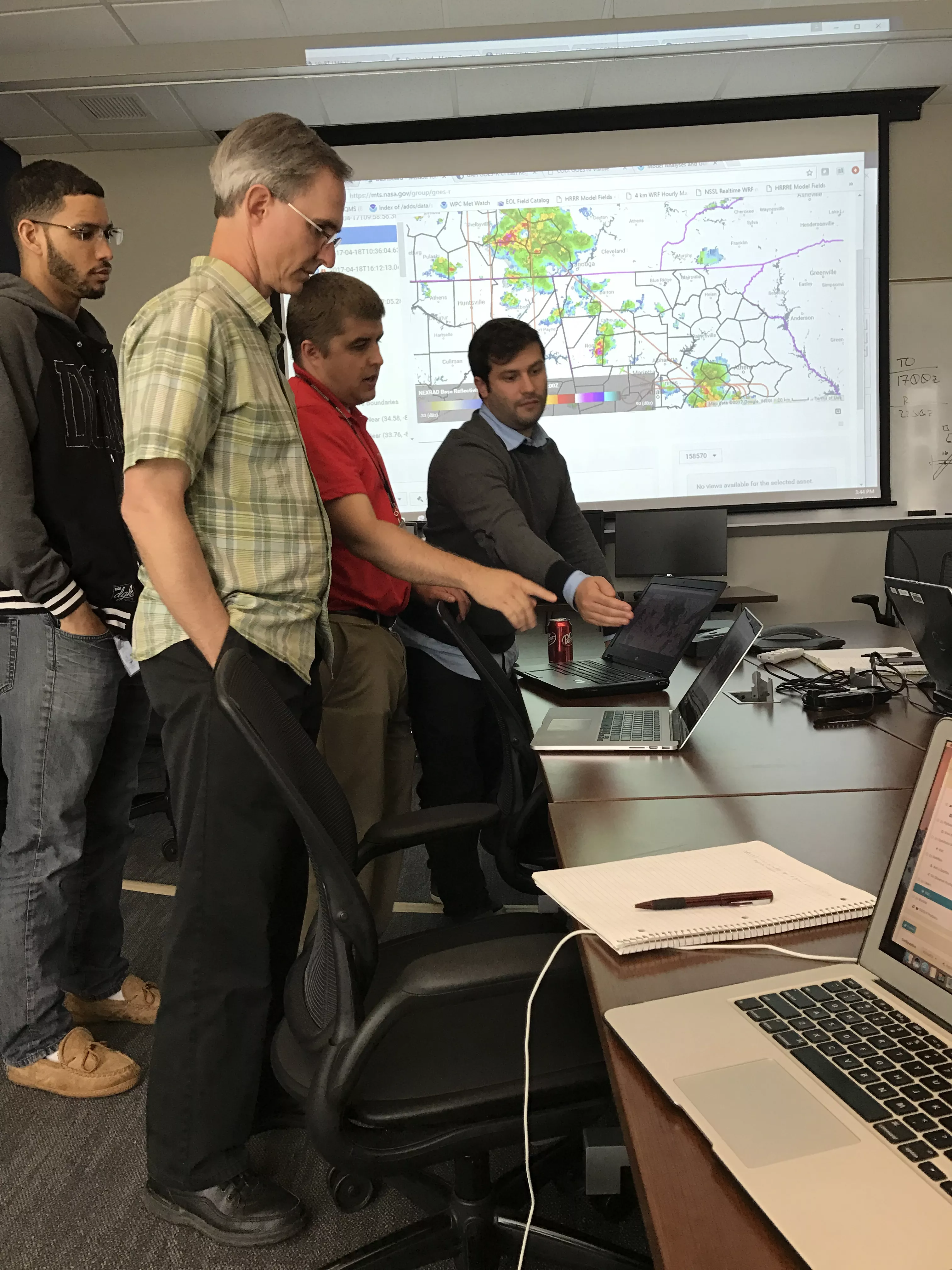 Group of forecasters standing around computer terminal. 