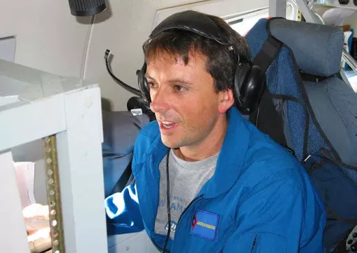 Image of man, Jason Dunion, seated in cockpit of research airplane. He is wearing a headset and a joyous expression.